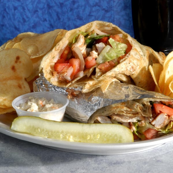Two chicken wraps with lettuce, tomato, and onion, served with chips, coleslaw, and a pickle.