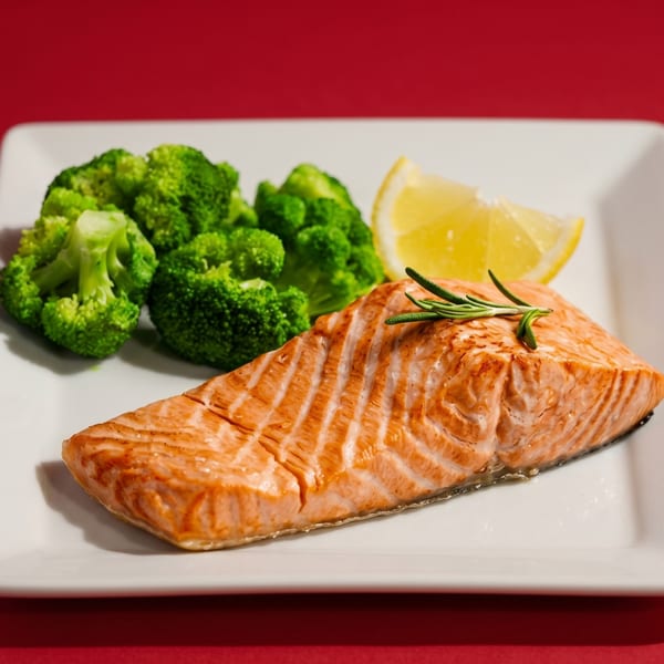 Grilled salmon fillet with rosemary, a lemon wedge, and steamed broccoli on a white plate.